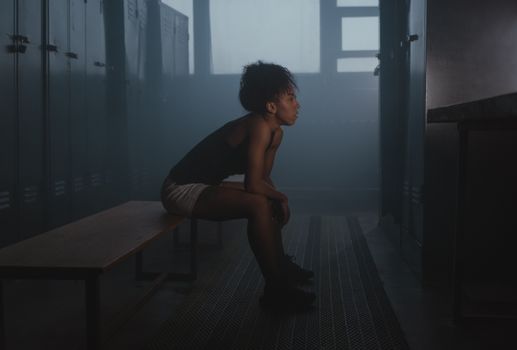 Woman sitting on a bench in a dimly lit locker room, exuding a pensive mood.