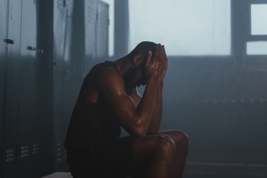 Sweaty man resting on bench in dimly lit locker room, showing exhaustion and recovery.