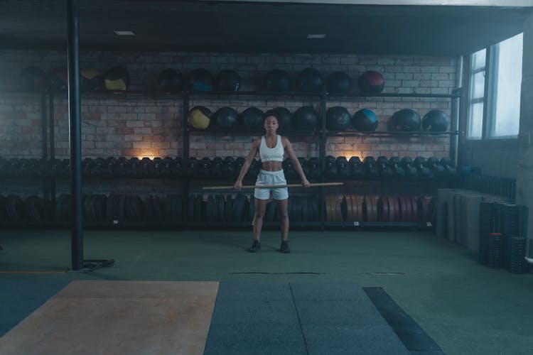 A Woman Holding A Barbell While Standing In The Gym