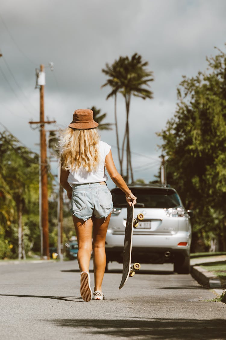 Back View Of A Woman Walking While Holding Her Skateboard