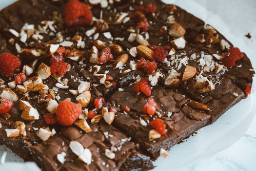 Close-up of rich chocolate brownies topped with raspberries and almonds.