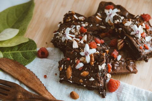 Free Rich chocolate brownies topped with raspberries, nuts, and flowers on a wooden table. Stock Photo