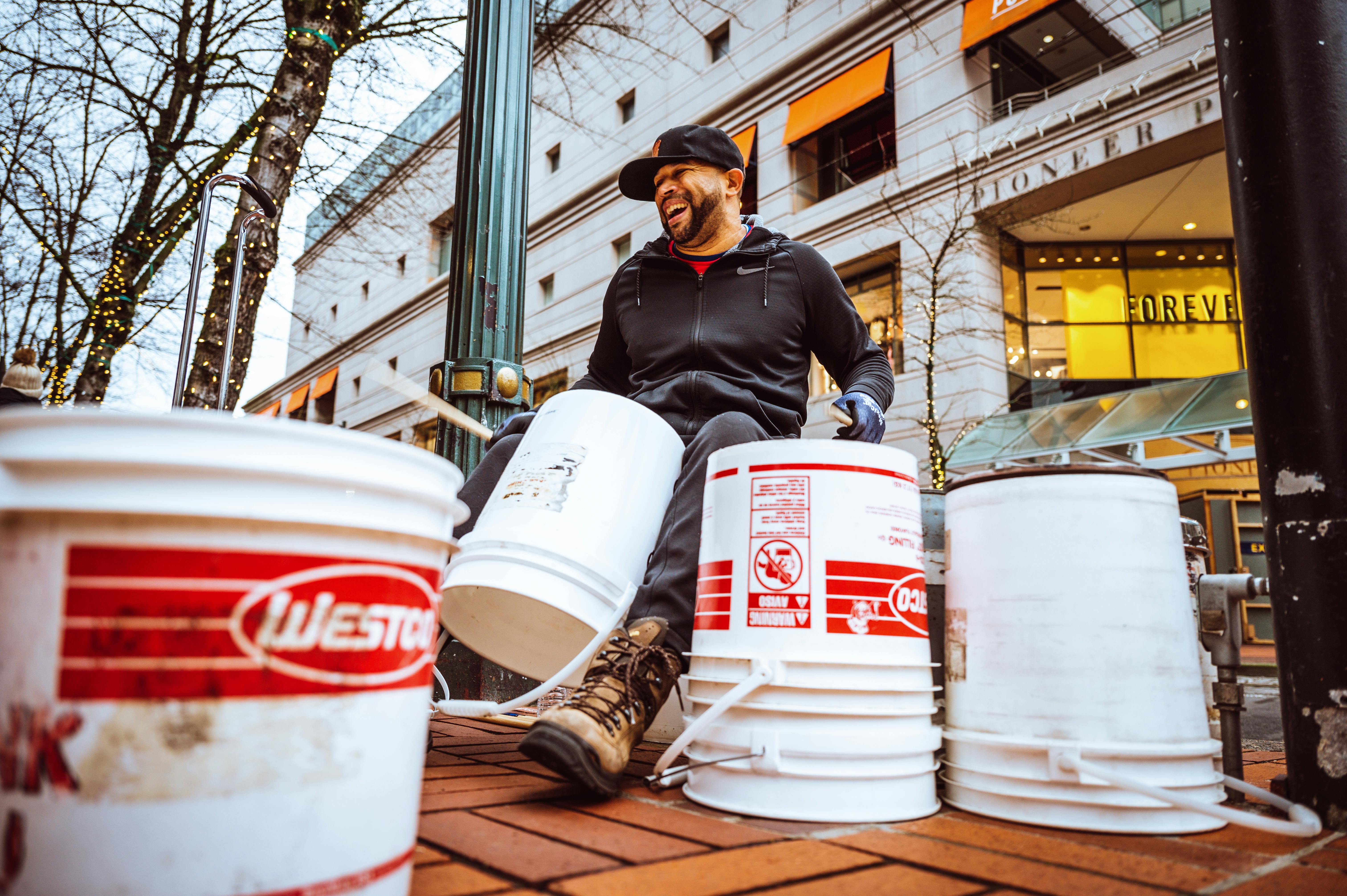 joyful creative ethnic busker using buckets during performance on city street