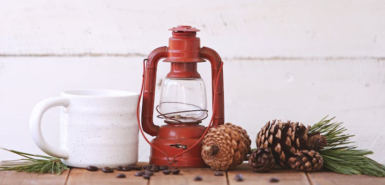 Red Kerosene Lantern Beside White Ceramic Mug On Brown Wooden Table