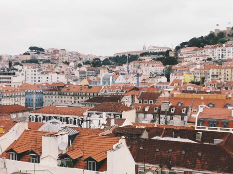 Panoramic view of Lisbon's historic rooftops and architecture under cloudy skies.