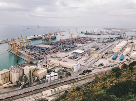 An aerial view of a busy industrial cargo port with cranes, containers, and ships.