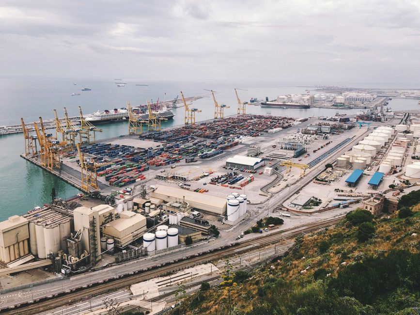 Una vista aérea de un ocupado puerto industrial de carga con grúas, contenedores y barcos.