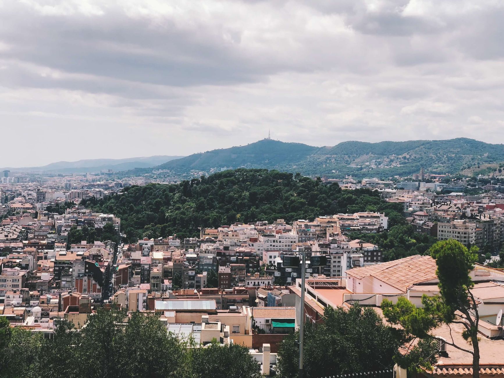 Explore the stunning panoramic view of Barcelona's vibrant cityscape with lush greenery and distant mountains.