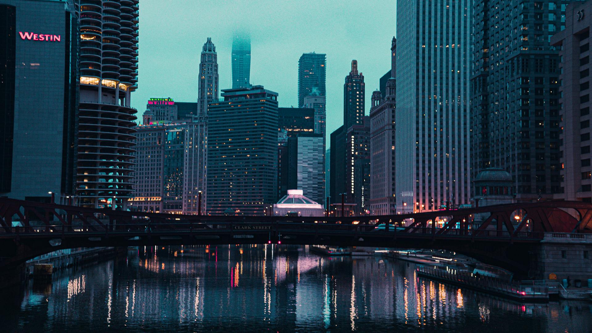 Moody evening skyline of Chicago featuring high-rise buildings and illuminated city lights around a river.