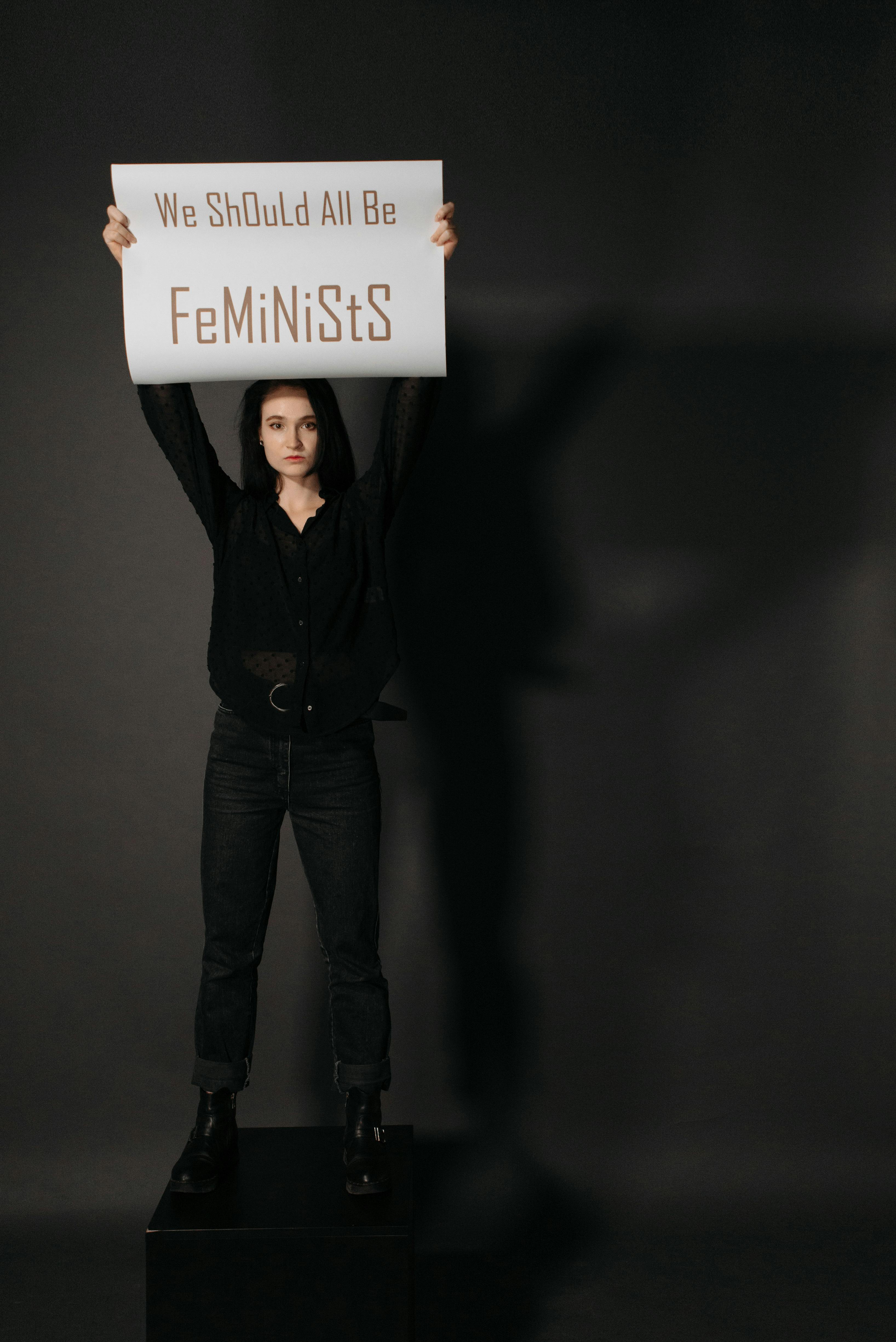 a woman in black long sleeves standing on a block while holding a poster