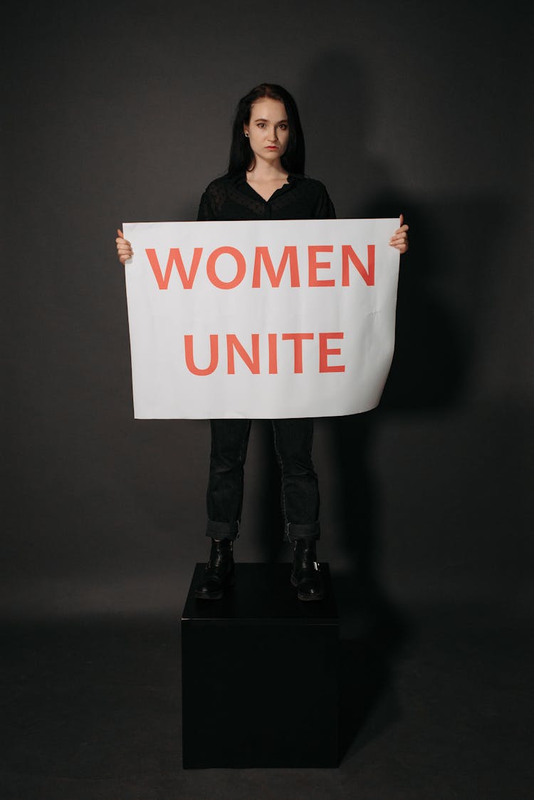 A Woman Standing On A Block While Holding A Poster