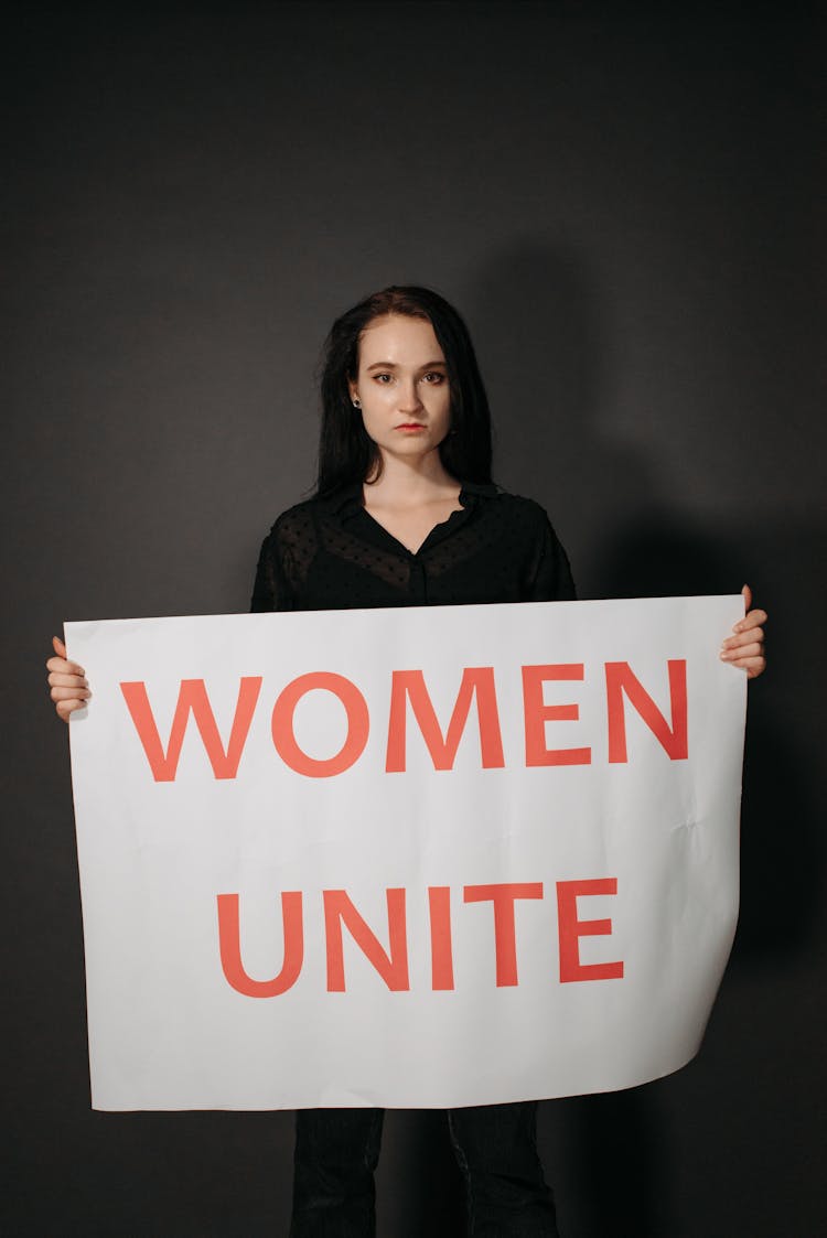 A Woman In Black Shirt Holding A Poster While Looking With A Serious Face