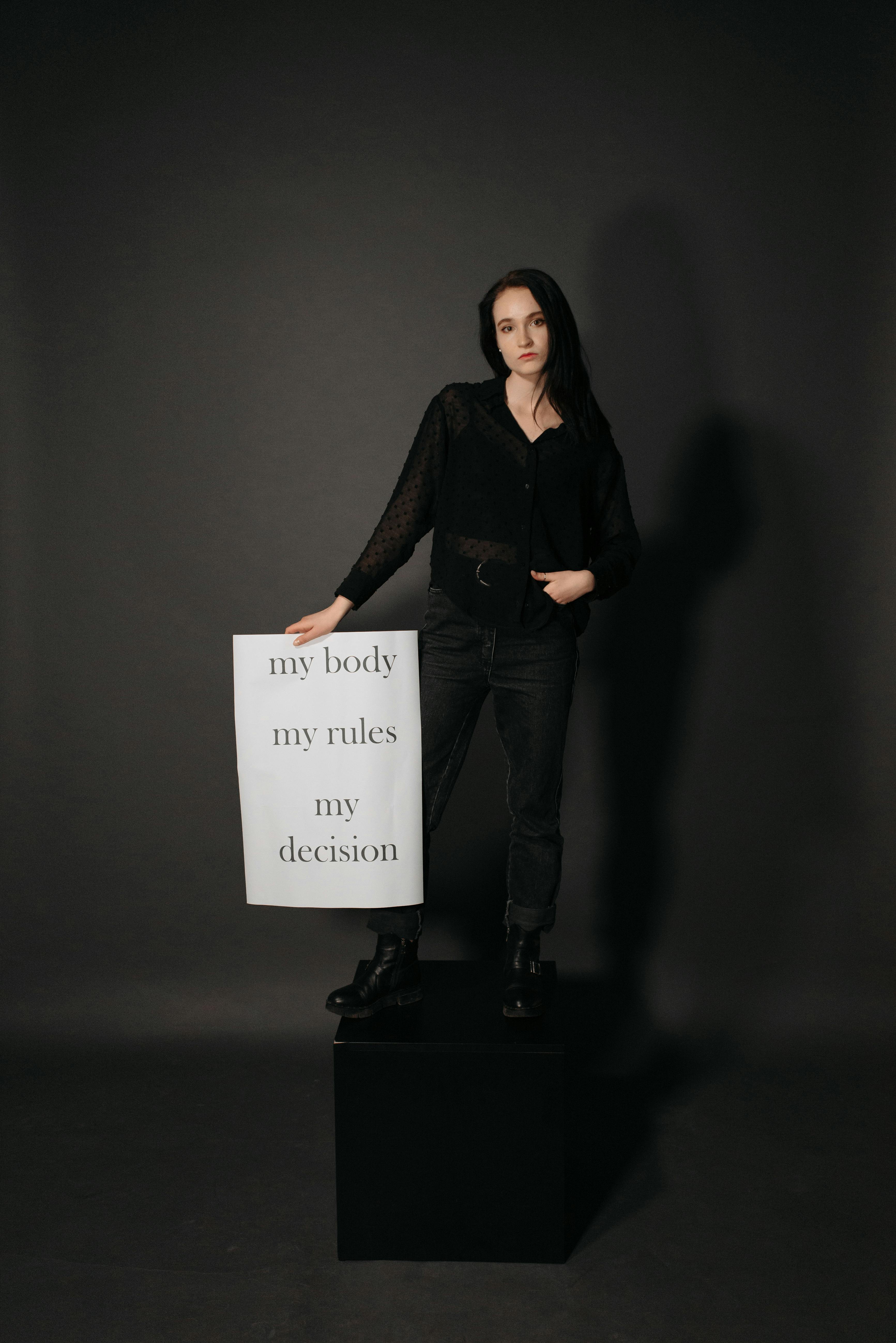 a woman in black clothes standing on a block while holding a poster