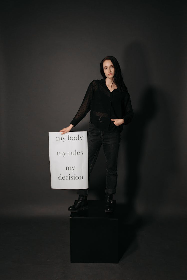 A Woman In Black Clothes Standing On A Block While Holding A Poster