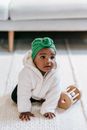 Curious adorable infant Indian girl wearing green turban crawling around white carpet with wooden sensory toy and looking away