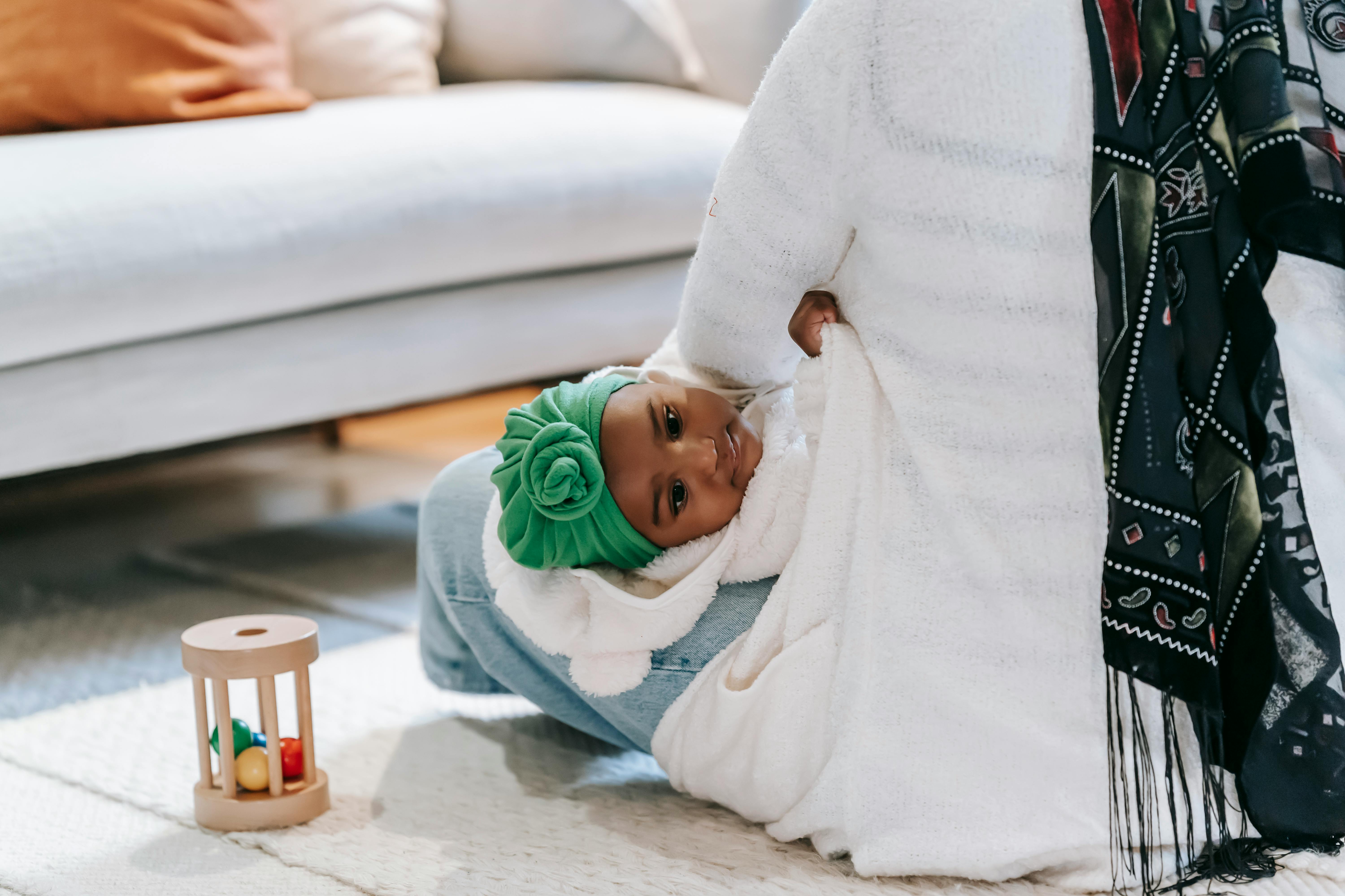 Back view of crop unrecognizable ethnic mother in casual clothes and traditional hijab hugging cute little girl while sitting on floor in cozy living room