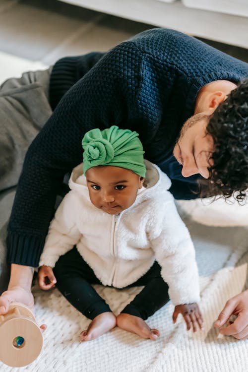 High angle of adorable little Indian child in turban sitting on floor while playing with crop young ethnic father at home