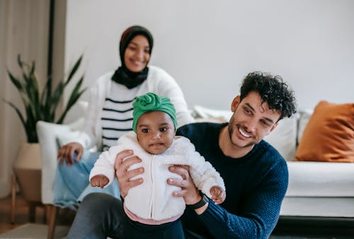 Happy diverse parents smiling while playing with cute baby in living room