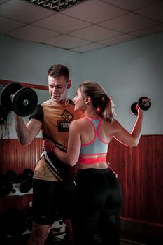 Active couple lifting dumbbells in a gym, embracing fitness and teamwork.