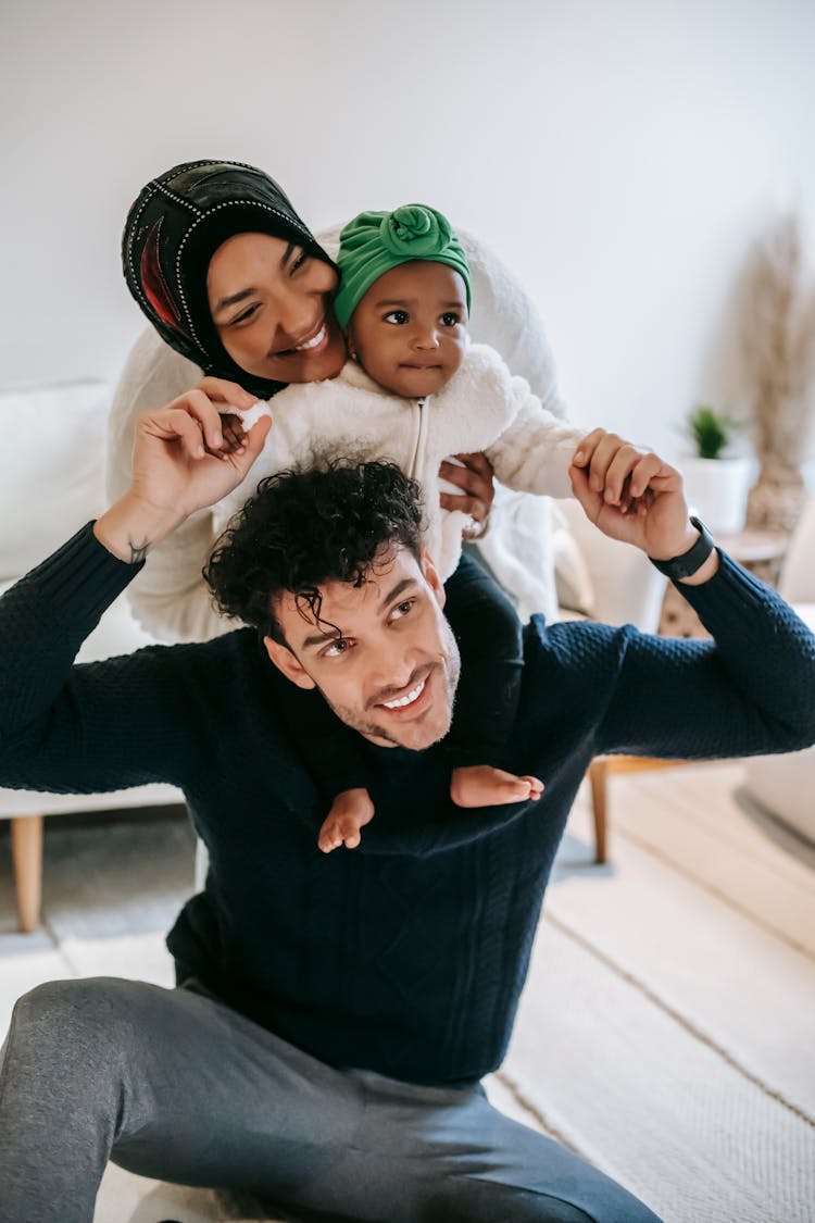 Happy Muslim Mother Embracing Black Baby Sitting On Father