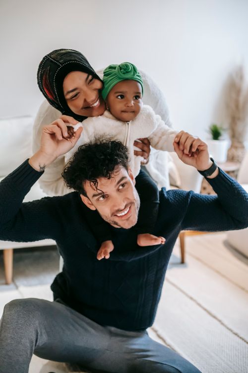 Free Delighted African American mother hugging adorable daughter sitting on shoulders of father while spending time together Stock Photo