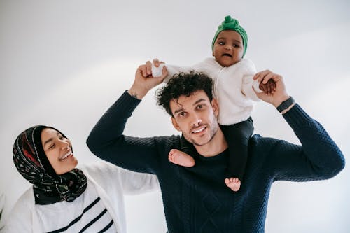 Smiling father standing with baby on shoulders near mother