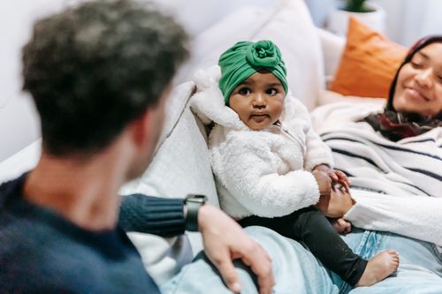 Free High angle of cute African American baby girl sitting on ethnic mother lying on sofa with dad Stock Photo