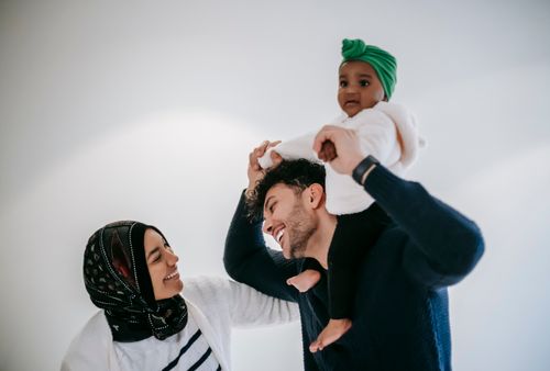 Free Happy father holding hands with black daughter sitting on shoulders while standing near cheerful mother against white background Stock Photo