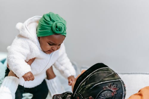 Free Muslin mom in hijab raising African American baby wearing turban and enjoying motherhood at home Stock Photo
