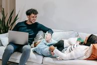 Smiling dad using netbook sitting on sofa near ethnic mom in hijab cuddling daughter