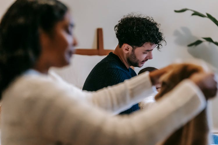 Father Sitting With Baby Near Black Mother Organizing Clothes