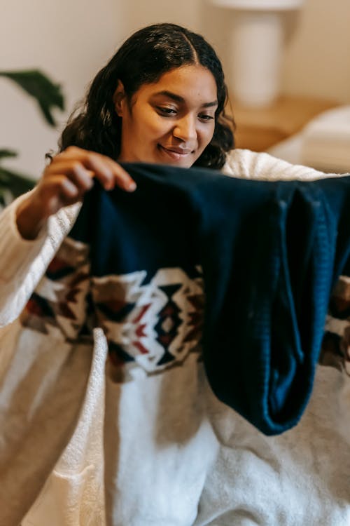 Free Young positive African American housewife with knitted sweater in hands doing household chores at home Stock Photo
