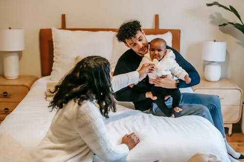 Free High angle of father cuddling African American upset baby while mother sitting close on bed in bedroom Stock Photo
