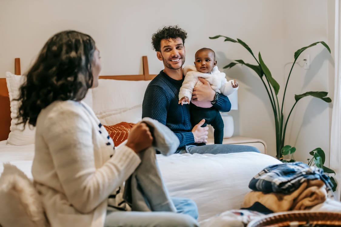 Free African American mother with clothes and ethnic father with newborn baby looking at each other while spending time in bedroom Stock Photo