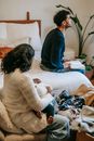 Side view of calm African American mother with newborn baby sitting near ethnic father on bed with book while spending time together at home