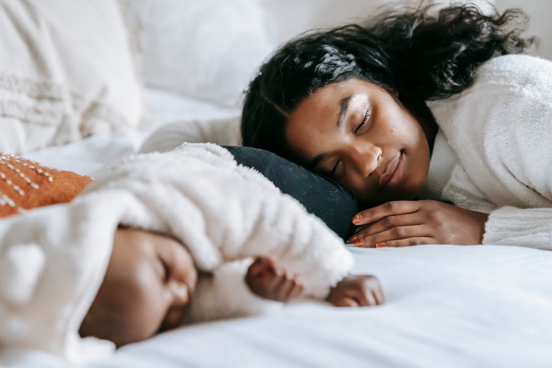Free African American woman and infant baby lying on bed with white blanket while sleeping peacefully together during bed time at home Stock Photo