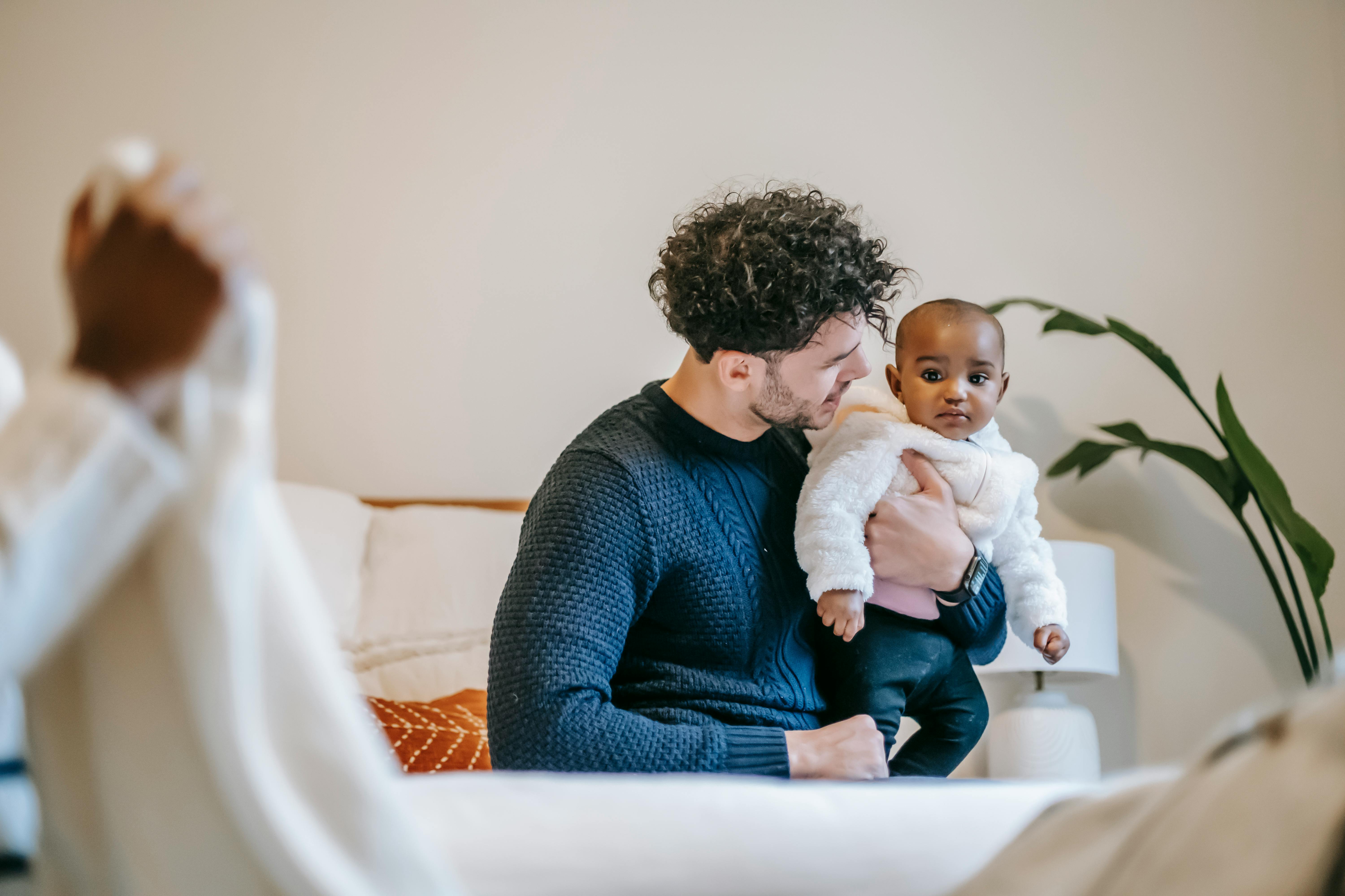 happy father embracing cute ethnic infant sitting on couch at home