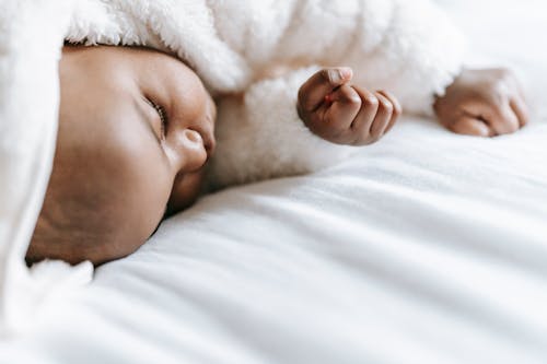 Free Adorable ethnic newborn baby in soft warm clothes sleeping on comfortable bed in daylight Stock Photo