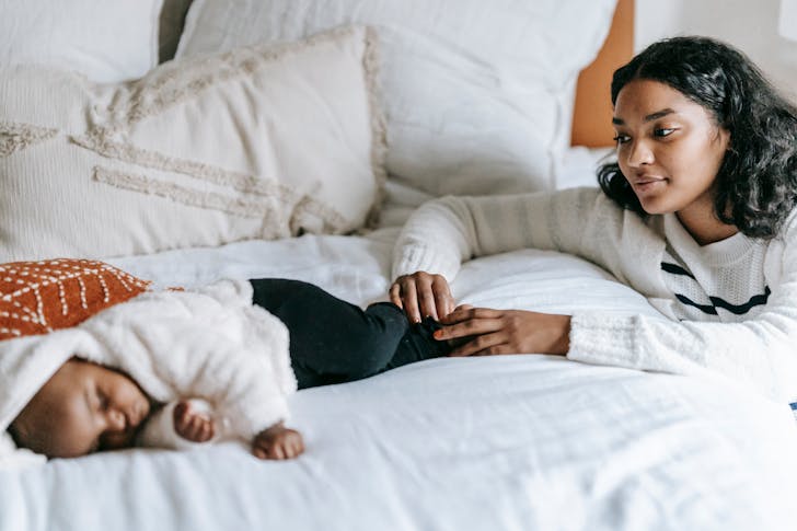 Calm young black woman looking at sleeping baby in bedroom
