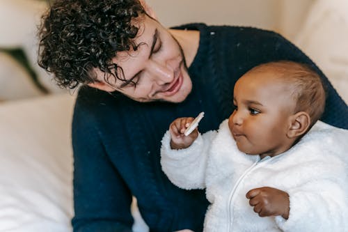 Smiling young man cuddling adorable little ethnic child in bedroom