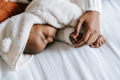 From above of crop anonymous ethnic mother embracing adorable newborn baby in warm clothes sleeping in bed in morning