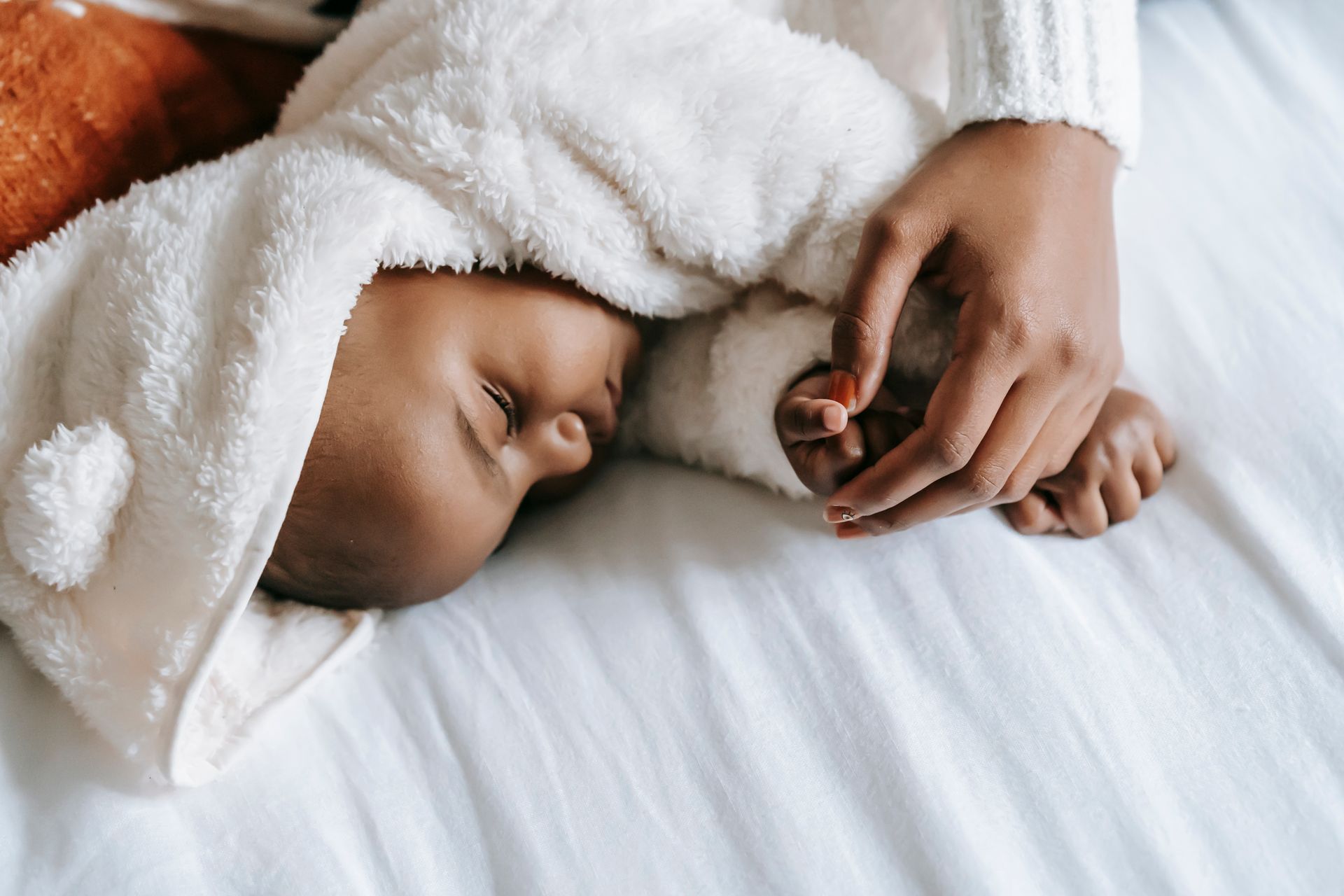 From above of crop anonymous ethnic mother embracing adorable newborn baby in warm clothes sleeping in bed in morning