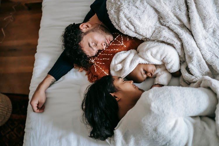 Diverse Family With Infant Sleeping On Bed