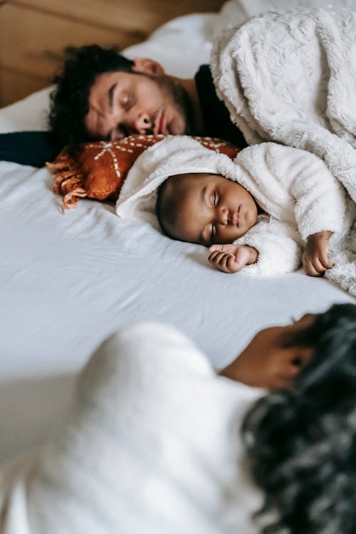Anonymous ethnic woman resting near husband and baby sleeping on bed