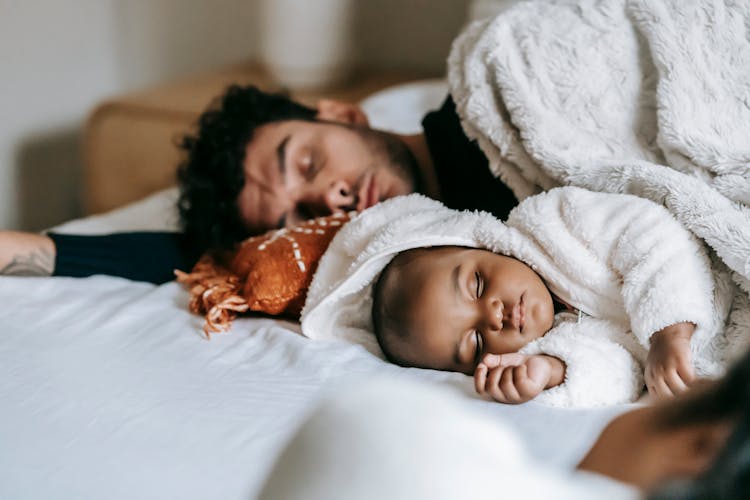 Unrecognizable Ethnic Mother Relaxing Near Baby Sleeping With Father On Bed