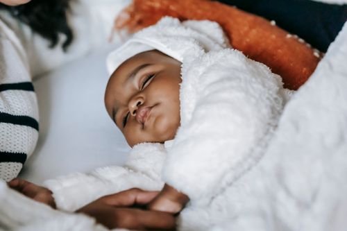 Free From above of crop anonymous African American mother holding hand of cute newborn baby in warm clothes sleeping on cozy bed Stock Photo