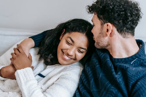 Free Crop enamored young man kissing head of happy ethnic girlfriend while embracing each other and resting in sofa at home Stock Photo