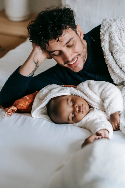 Happy ethnic father on bed with black infant