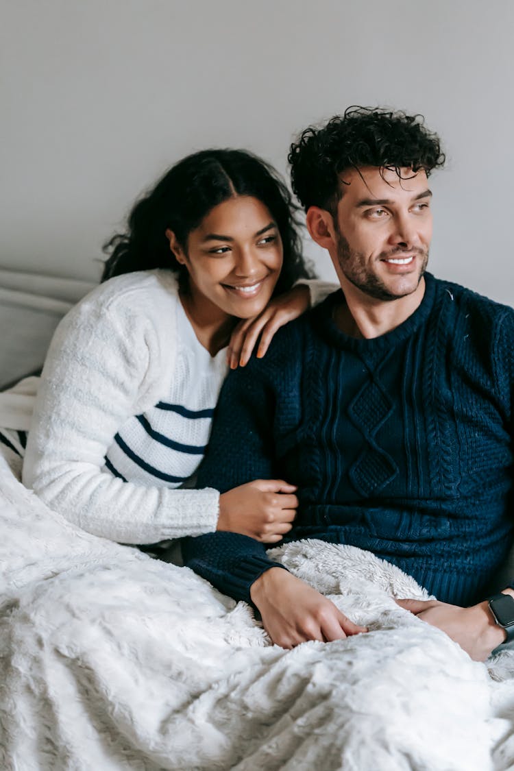 Positive Multiracial Couple Sitting On Couch Under Blanket