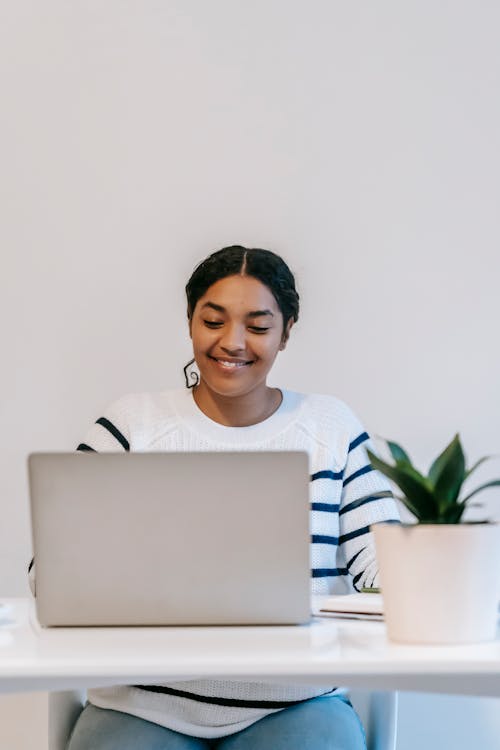 Free Ethnic lady working remotely on netbook at table in room Stock Photo